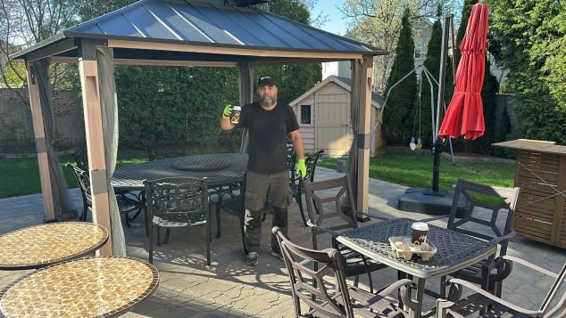 Man holding drink in backyard gazebo.